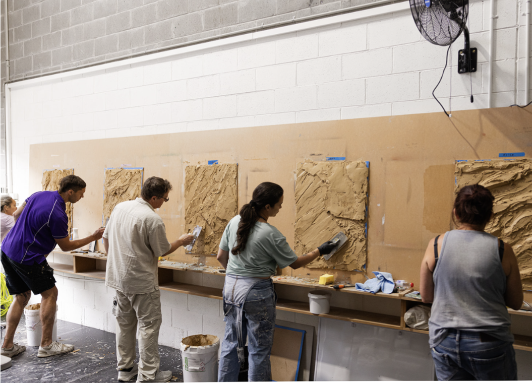 Trainees applying textured plaster to practice panels at a training workshop