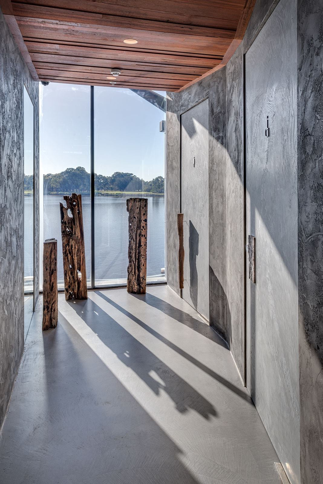 Waterfront corridor with grey microcement walls and floor and reclaimed timber posts
