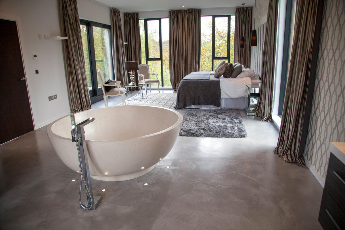 Bedroom suite with a seamless grey microcement floor and a freestanding bath