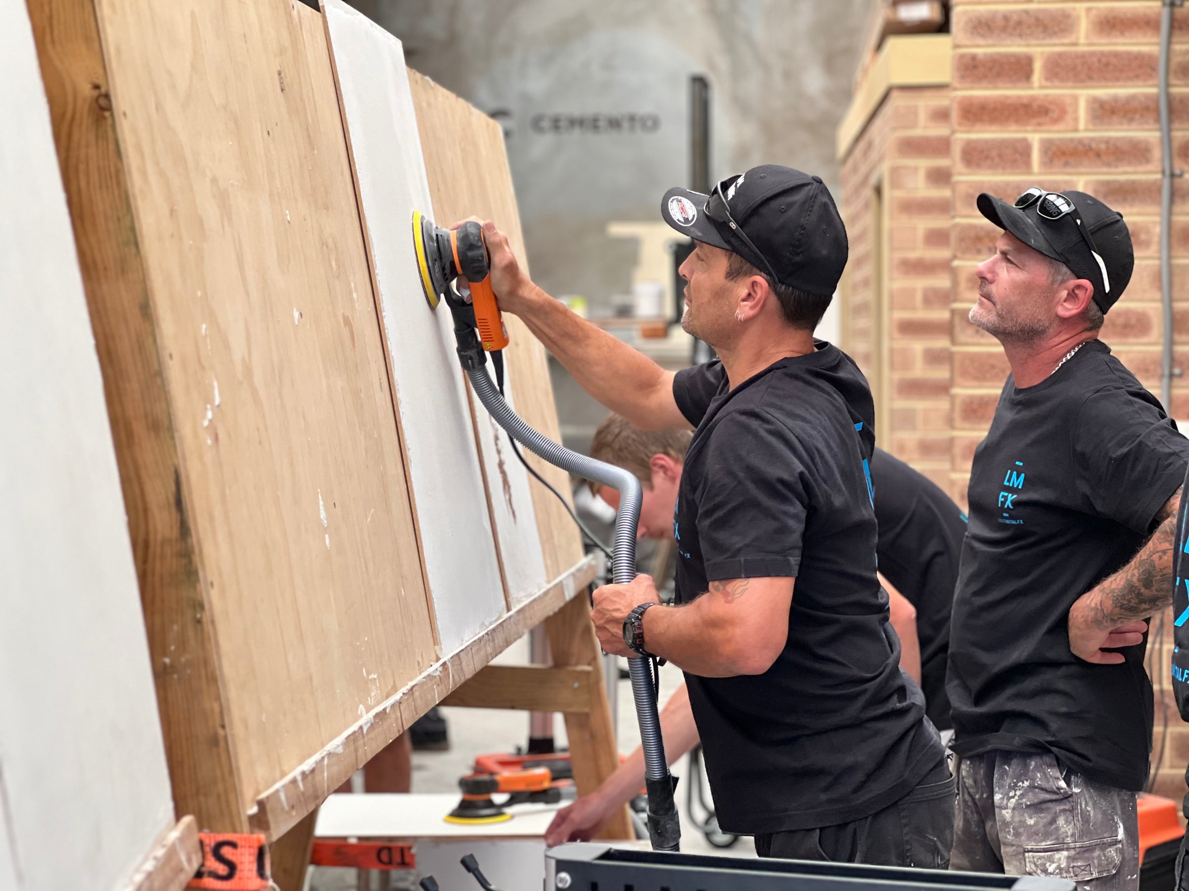 Trainees sanding a practice panel with an orbital sander during a course