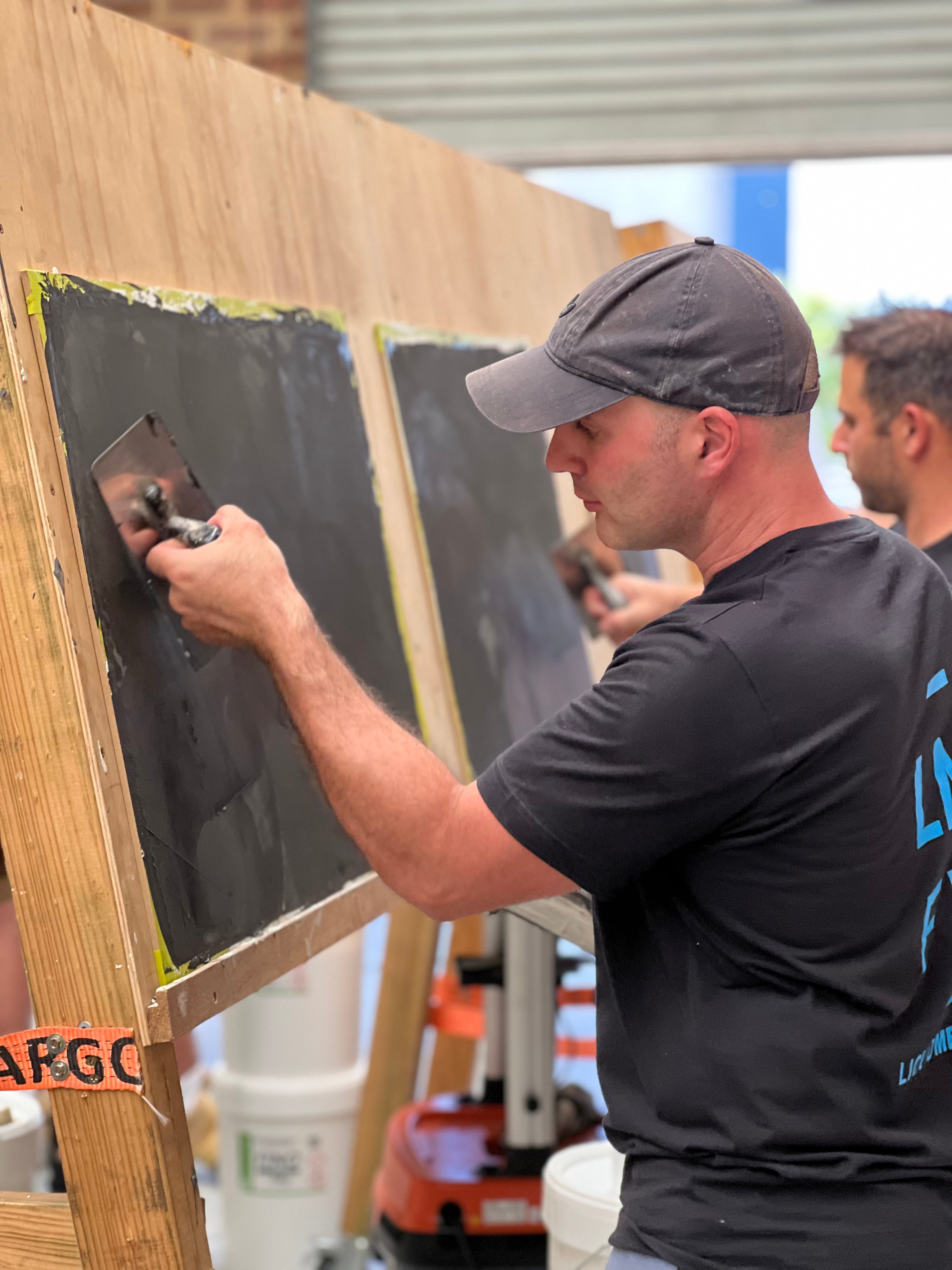 Trainee applying a dark microcement coat to a practice board with a trowel