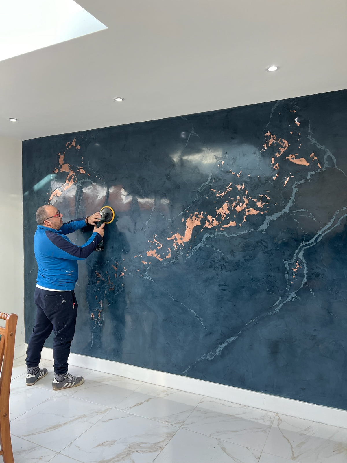 Applicator polishing a navy marble-effect plaster wall with copper veining