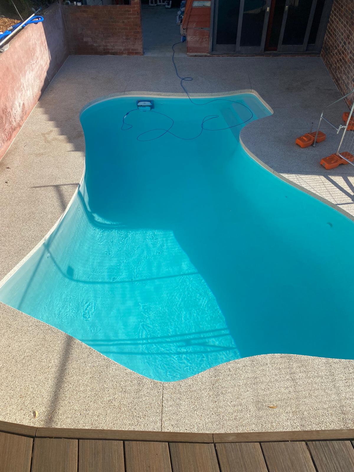 Freeform turquoise pool with seamless microcement interior and speckled stone deck